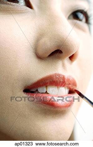 Stock Image - Woman putting on lipstick with lip brush, close up. Fotosearch