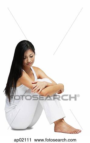 Stock Image - Woman sitting on floor, hugging knees, looking down. Fotosearch