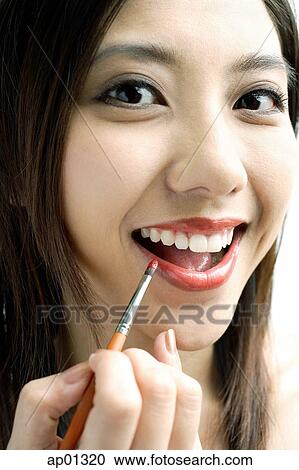 Stock Image - Woman smiling at camera, putting on lipstick with lip brush. Fotosearch