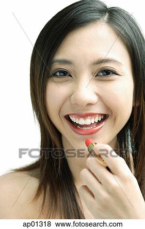 Stock Photo - Woman smiling at camera, putting on lipstick. Fotosearch