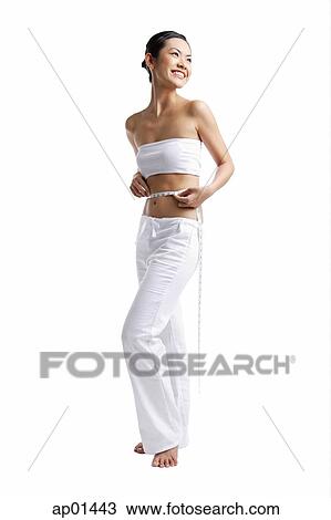 Woman standing and holding tape measure around waist, smiling View Large Photo Image Stock Image - Woman standing and holding tape measure around waist, smiling. Fotosearch