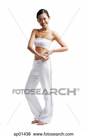 Stock Photo - Woman standing and holding tape measure around waist. Fotosearch