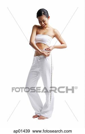 Woman standing and holding tape measure around waist, looking down View Large Photo Image Stock Photo - Woman standing and holding tape measure around waist, looking down. Fotosearch