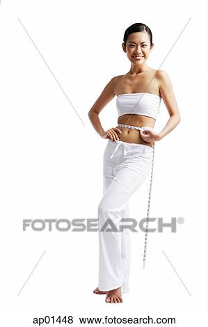 Woman standing and holding tape measure around waist, smiling View Large Photo Image Stock Photo - Woman standing and holding tape measure around waist, smiling. Fotosearch
