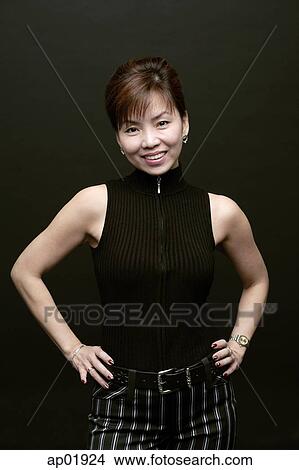 Picture - Woman standing, hands on hips, smiling at camera. Fotosearch