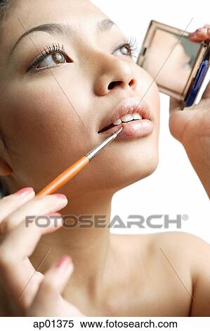 Stock Photography - Woman using lipstick brush and holding compact mirror. Fotosearch