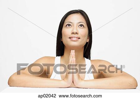 Stock Image - Woman with hands together, looking up, smiling. Fotosearch