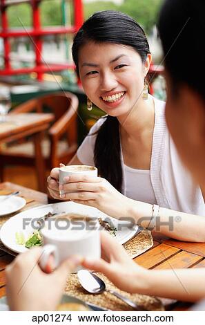Picture - Women eating out, holding cups of coffee. Fotosearch