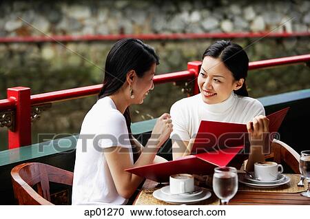 Stock Image - Women in cafe, looking at menu, laughing. Fotosearch