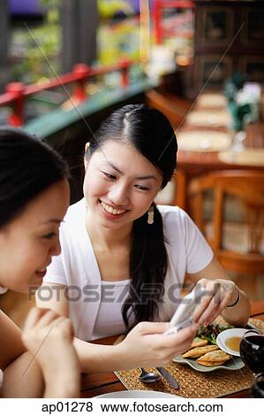 Stock Photo - Women sitting in cafe, looking at mobile phone. Fotosearch