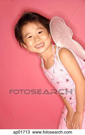 Stock Image - Young girl in pink dress with artificial wings, smiling at camera. Fotosearch