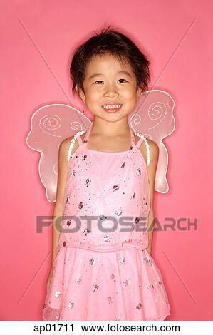 Stock Image - Young girl in pink dress with wings attached, looking at camera. Fotosearch
