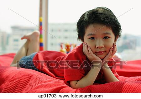 Stock Image - Young girl lying on sofa, looking at camera, hands on face. Fotosearch