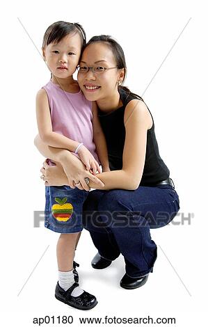 Stock Image - Young girl standing, mother crouching next to her, looking at camera. Fotosearch