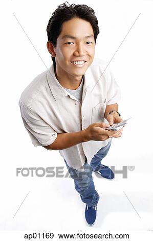 Young man holding mobile phone, looking up at camera View Large Photo Image Stock Photo - Young man holding mobile phone, looking up at camera. Fotosearch