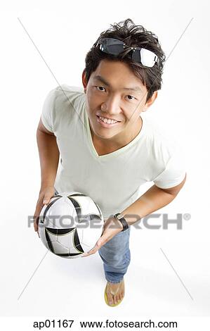 Young man in T-shirt and jeans, holding soccer ball, smiling at camera View Large Photo Image Stock Photo - Young man in T-shirt and jeans, holding soccer ball, smiling at camera. Fotosearch