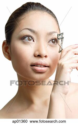 Stock Image - Young woman holding eyelash curler near eye. Fotosearch