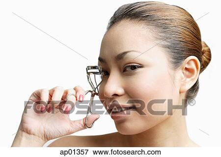 Stock Photo - Young woman holding eyelash curler, looking at camera. Fotosearch
