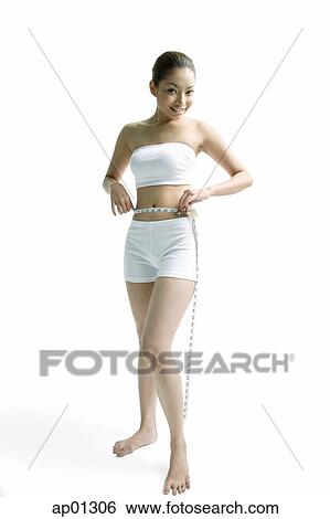 Young woman measuring her waist with measuring tape, smiling at camera View Large Photo Image Stock Photograph - Young woman measuring her waist with measuring tape, smiling at camera. Fotosearch