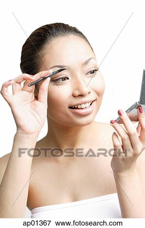 Stock Photo - Young woman using eyebrow brush, looking away. Fotosearch