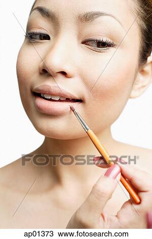 Stock Image - Young woman using lipstick brush, portrait. Fotosearch