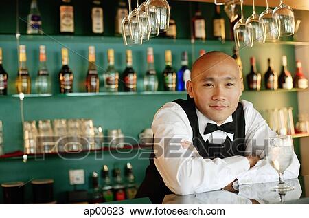 Stock Image - Bartender behind bar counter, glass of water in front of him. Fotosearch
