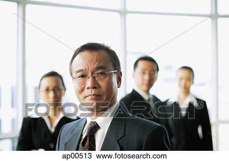 Stock Image - Businessman looking at camera, people in the background. Fotosearch