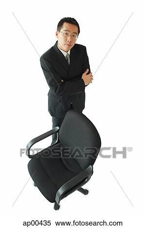 Businessman standing next to office chair, arms crossed View Large Photo Image Stock Photography - Businessman standing next to office chair, arms crossed. Fotosearch