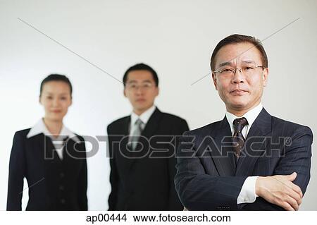 Picture - Businessman with arms crossed, looking at camera, two executives behind him. Fotosearch