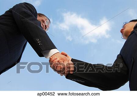 Stock Image - Businessmen shaking hands, low angle view. Fotosearch