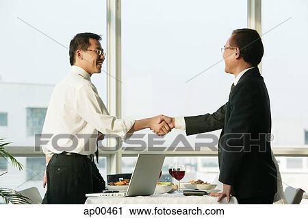 Stock Image - Businessmen shaking hands over lunch table. Fotosearch