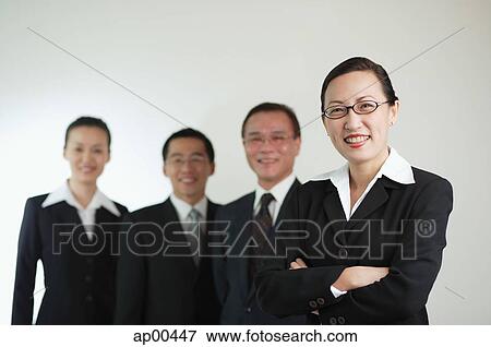 Businesswoman with arms crossed, other executives in the background, smiling View Large Photo Image Stock Photo - Businesswoman with arms crossed, other executives in the background, smiling. Fotosearch