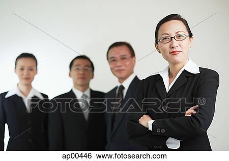 Stock Photograph - Businesswoman with arms crossed, other executives in the background. Fotosearch