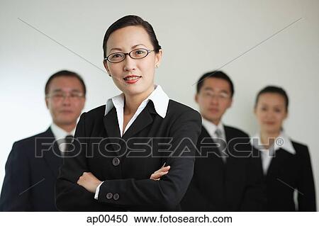 Stock Image - Businesswoman with arms crossed, people in the background. Fotosearch