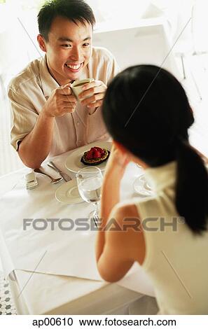 Stock Image - Couple at cafe, man holding coffee cup, facing woman. Fotosearch