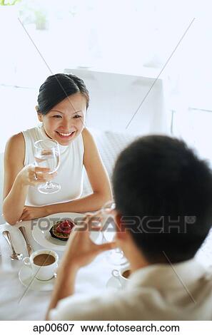 Couple at cafe, woman holding glass of water, high angle view View Large Photo Image Stock Photo - Couple at cafe, woman holding glass of water, high angle view. Fotosearch
