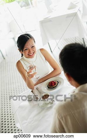 Stock Photo - Couple at cafe, woman holding glass of water. Fotosearch
