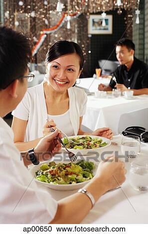 Stock Image - Couple eating at restaurant, people in the background. Fotosearch