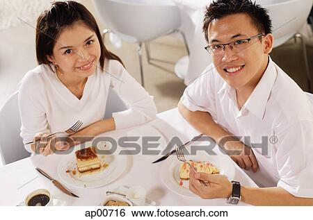 Couple eating dessert in restaurant, looking up at camera View Large Photo Image Stock Photograph - Couple eating dessert in restaurant, looking up at camera. Fotosearch