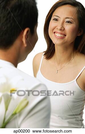 Couple facing each other, man with flowers behind his back, woman smiling View Large Photo Image Stock Image - Couple facing each other, man with flowers behind his back, woman smiling. Fotosearch
