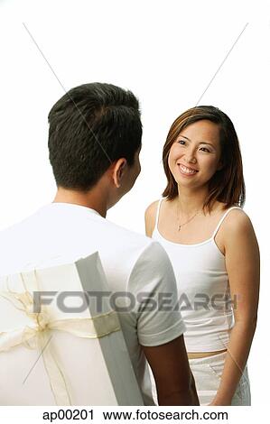 Couple facing each other, man with present behind his back, woman smiling View Large Photo Image Stock Image - Couple facing each other, man with present behind his back, woman smiling. Fotosearch