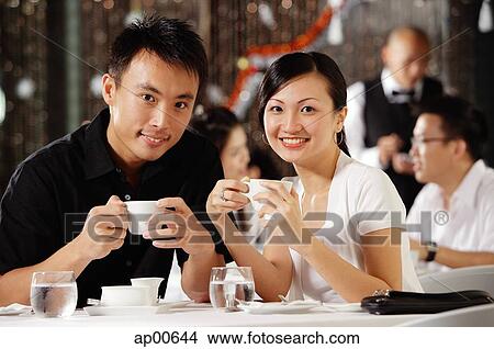 Picture - Couple in restaurant, holding cups, smiling at camera. Fotosearch