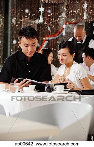 Stock Image - Couple in restaurant, looking through menu, people in the background. Fotosearch