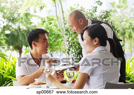 Stock Photo - Couple in restaurant, man giving waiter credit card. Fotosearch