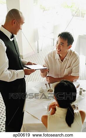 Couple in restaurant, man handing menu back to waiter View Large Photo Image Stock Photo - Couple in restaurant, man handing menu back to waiter. Fotosearch
