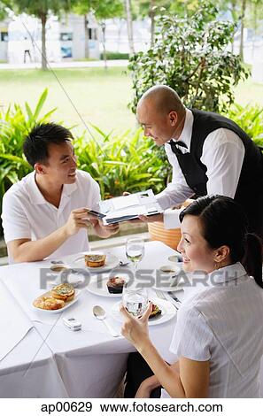 Couple in restaurant, man handing payment to waiter View Large Photo Image Stock Photo - Couple in restaurant, man handing payment to waiter. Fotosearch