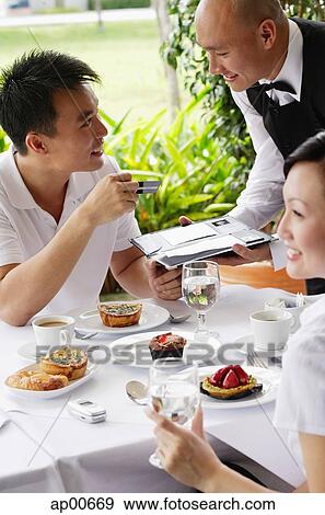Stock Photo - Couple in restaurant, man making payment with credit card. Fotosearch
