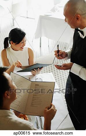 Stock Photography - Couple looking at menus, waiter taking their order. Fotosearch