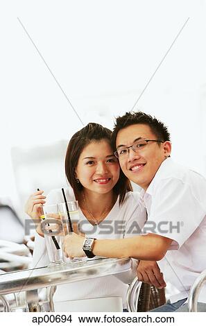 Couple sitting at table with drinks, looking at camera View Large Photo Image Picture - Couple sitting at table with drinks, looking at camera. Fotosearch