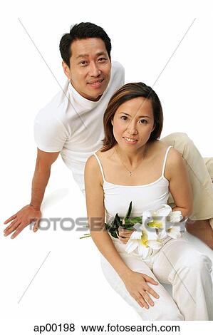 Stock Photo - Couple sitting on floor looking at camera, woman holding floral bouquet. Fotosearch